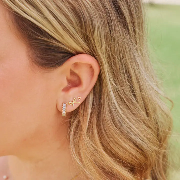 Medium Esther gold-tone huggie earring worn on an ear alongside small gold-tone studs.