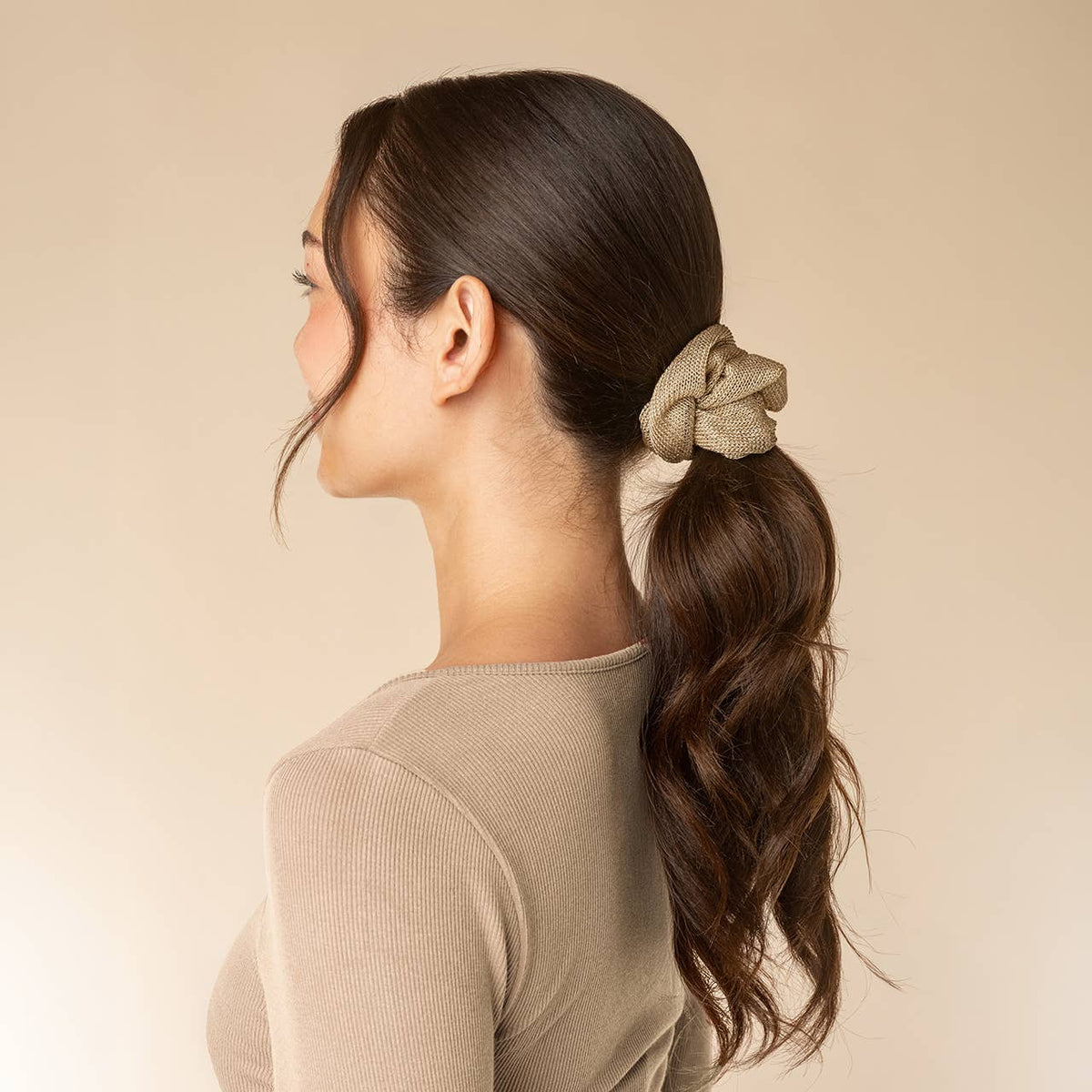 Kitsch gold metallic mesh scrunchie holding a low ponytail, side view