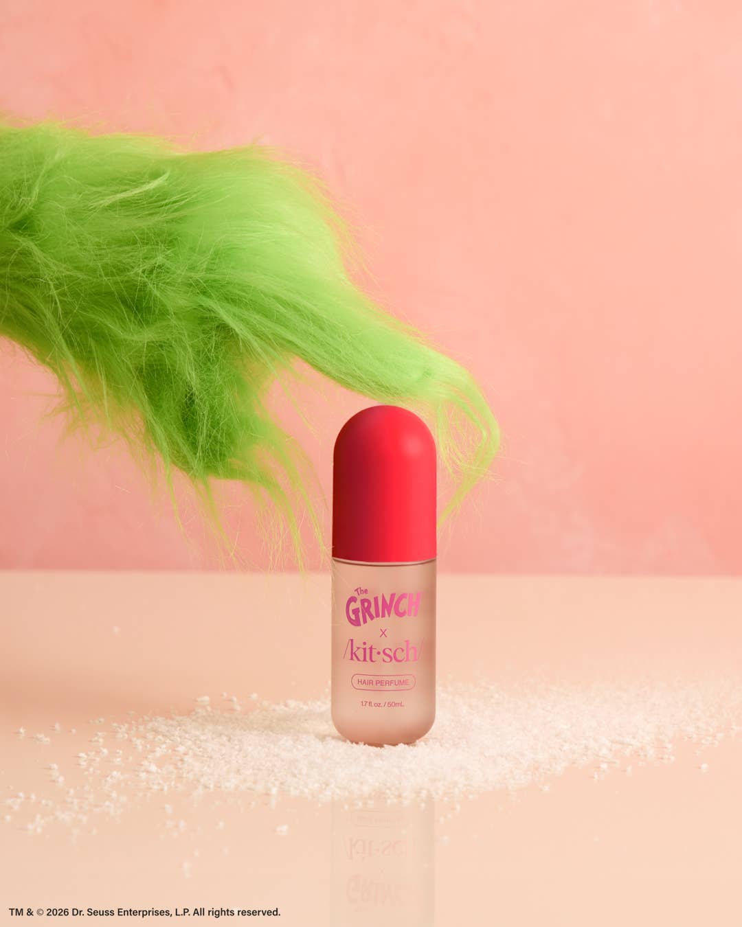The Grinch x Kitsch Cherry Cheer hair perfume bottle beside green faux fur on pink