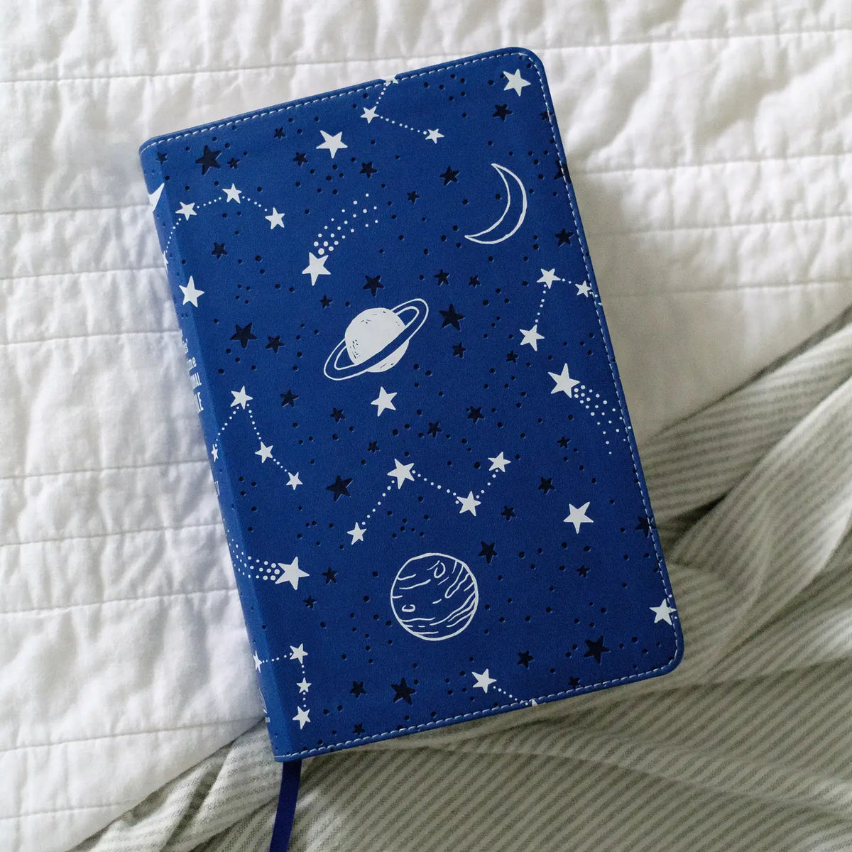 Kids' Bedtime Devotional Bible, navy star and planet cover on a bed