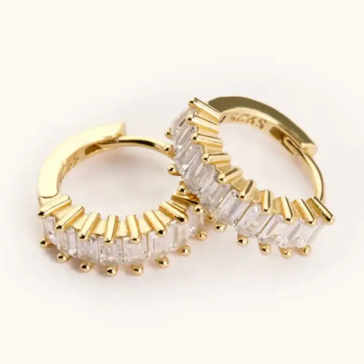 Medium Esther gold-tone huggie hoop earrings with clear rectangular stones, shown overlapping on a light background.