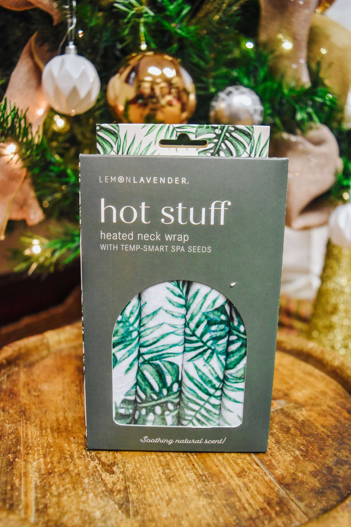Lemon Lavender Hot Stuff Heated Neck Wrap in green leaf print, boxed by a Christmas tree