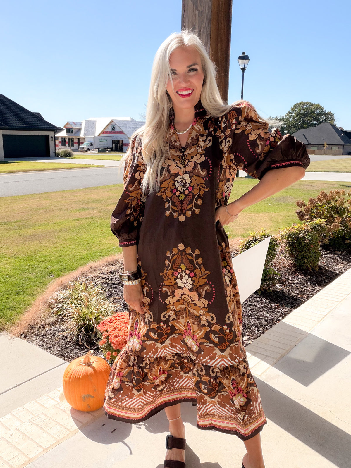 Model laughing in a brown border floral print midi dress with puff sleeves, styled with white sneakers