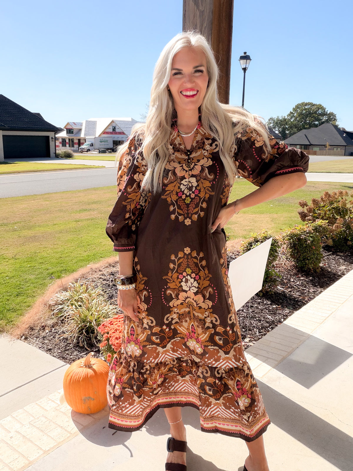 Model poses with hand on hip wearing a brown floral midi dress with a scalloped ruffle border hem