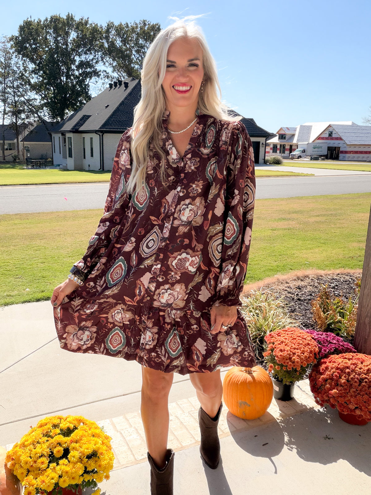 Model holding the ruffled hem of a merlot floral button-down dress with relaxed long sleeves
