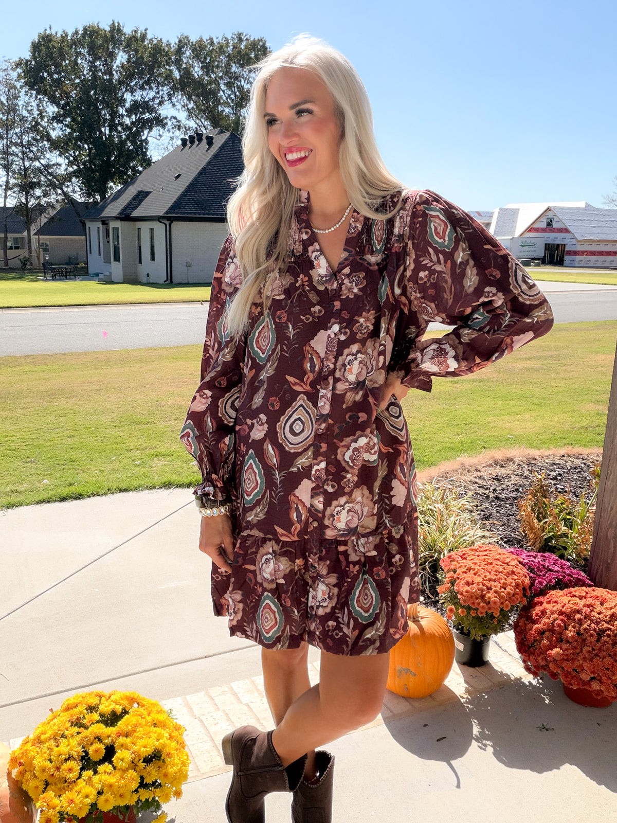 Angled front view of merlot floral smocked dress, model posing with one hand on hip and dark boots