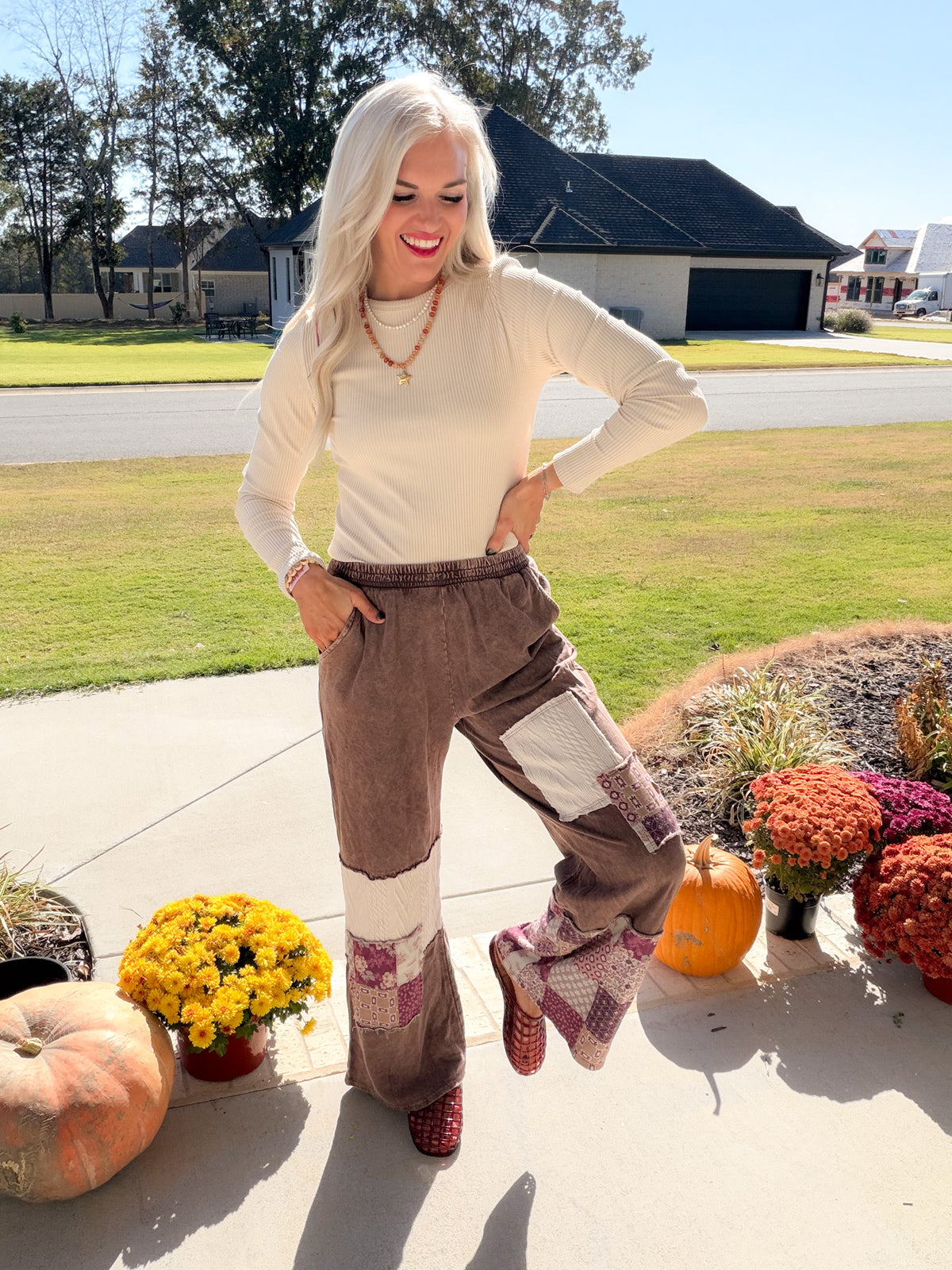 Model lifting one leg in chocolate paisley patchwork pants, showing the wide-leg cut and contrasting panels.