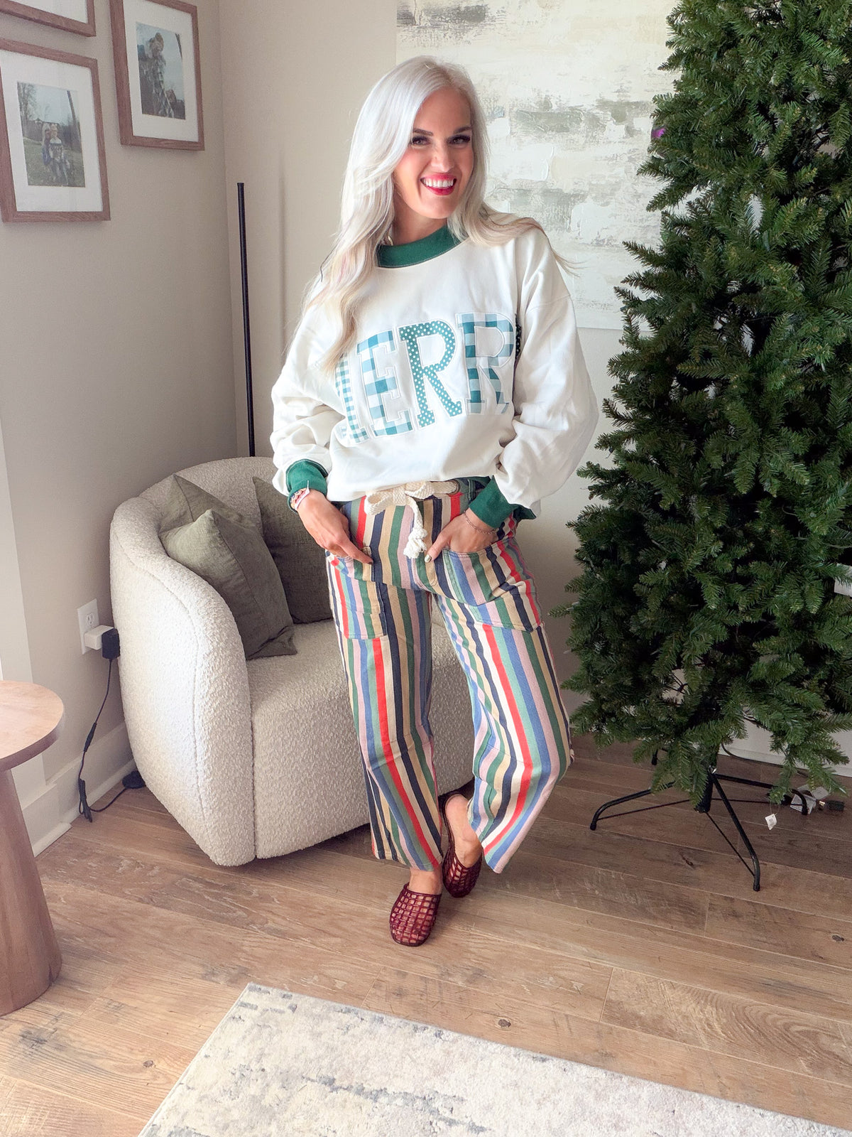 Women's ivory MERRY Christmas sweatshirt with green collar and cuffs, styled with striped pants and woven mules.