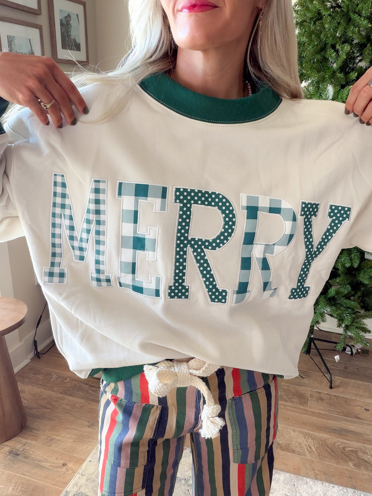 Close-up of plaid and polka dot MERRY letter appliqués and green mock neckline on an ivory Christmas sweatshirt.