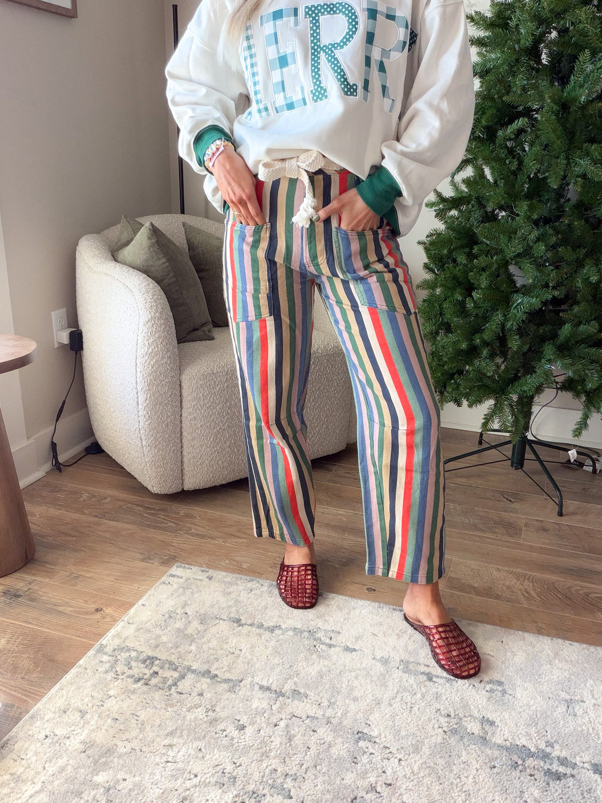 Women's multi stripe relaxed fit jeans showing the rope waist tie and front square pockets, styled with woven mules.