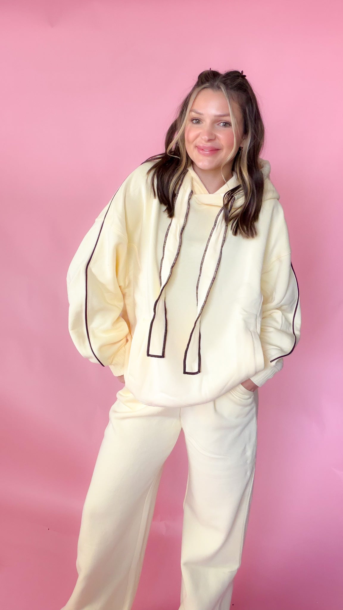 woman standing against pink background with yellow hoodie and sweatpants matching set