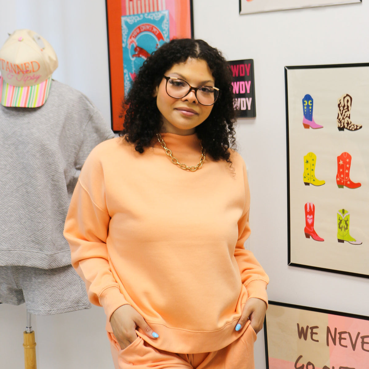 Woman in a green sweater and checkered pants standing in a room with pink couch, decorative pillows, and wall art.