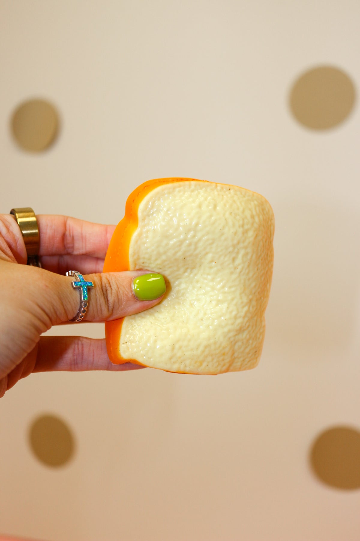 Close-up of a hand pressing a toast-shaped squishy with a cream-colored center and golden-orange crust.