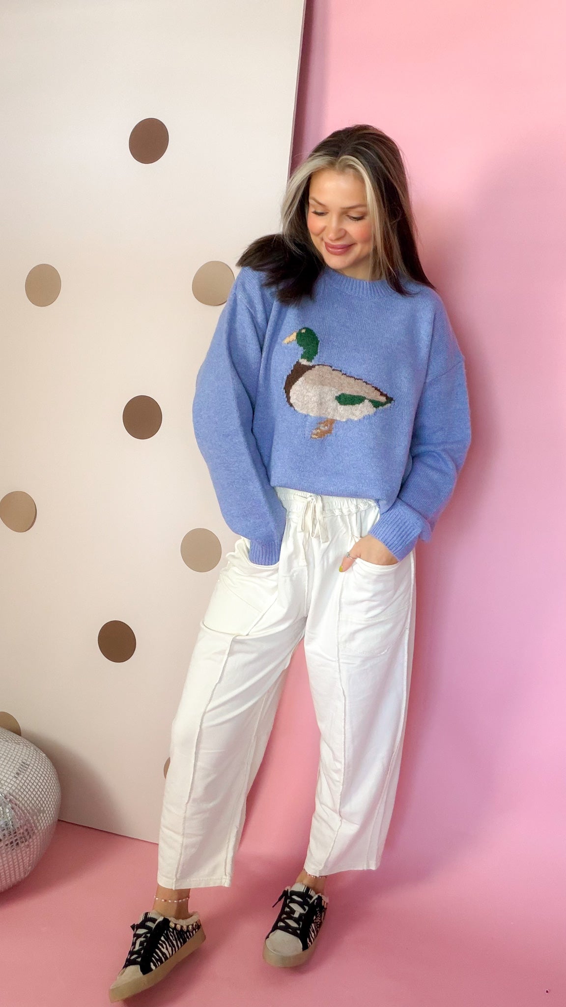 Women's coastal blue mallard duck sweater paired with white pants and patterned sneakers, front view.
