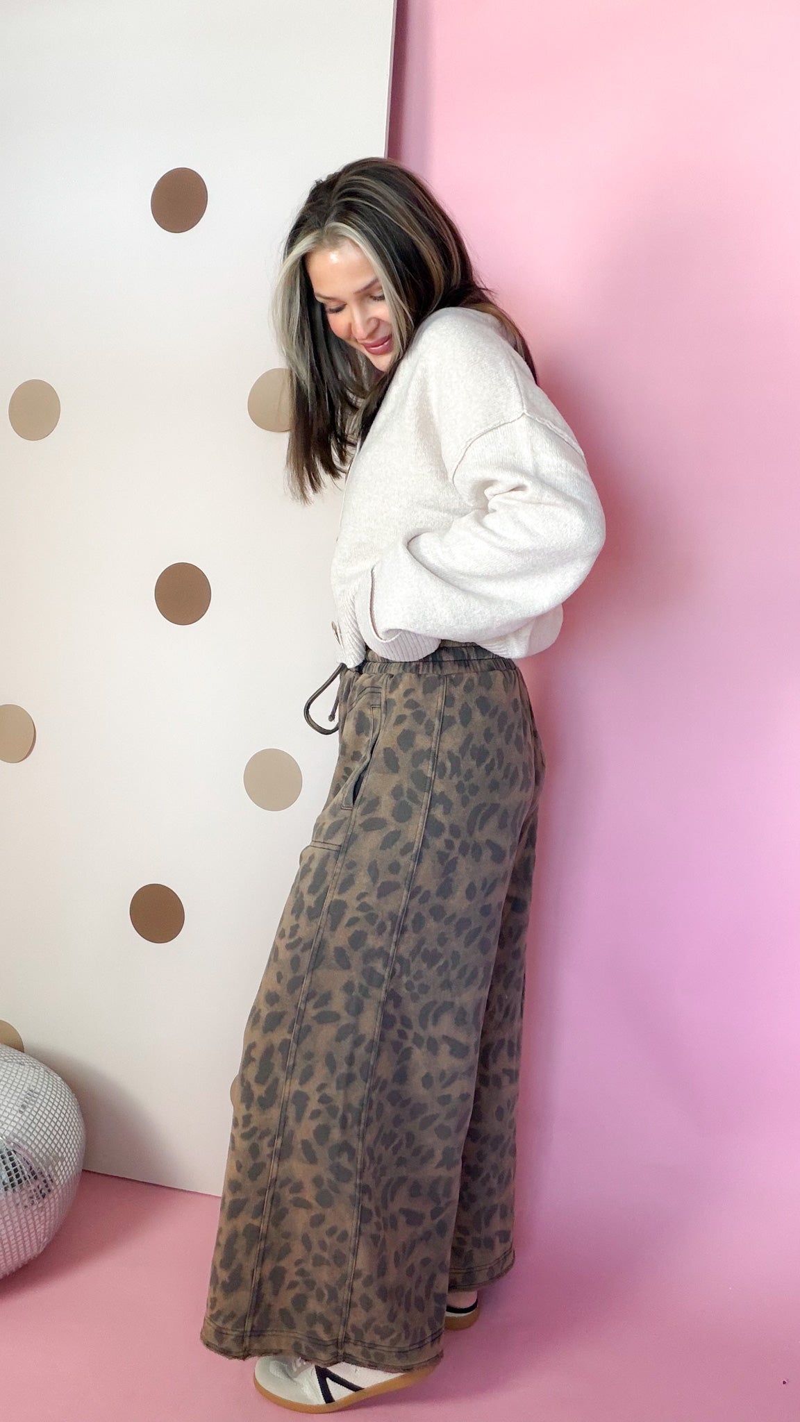 Side view of mocha leopard pants showing the wide-leg shape, styled with a cream cardigan and sneakers.