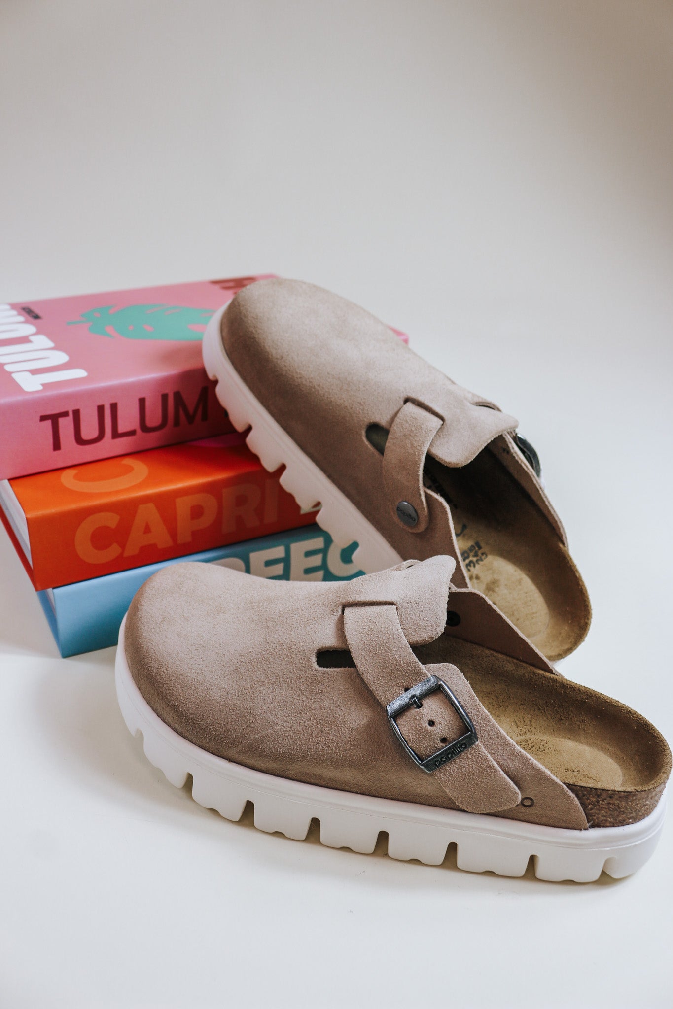 A pair of brown Birkenstock chunky platform clogs resting on stacked books, showcasing the upper part of the shoes.