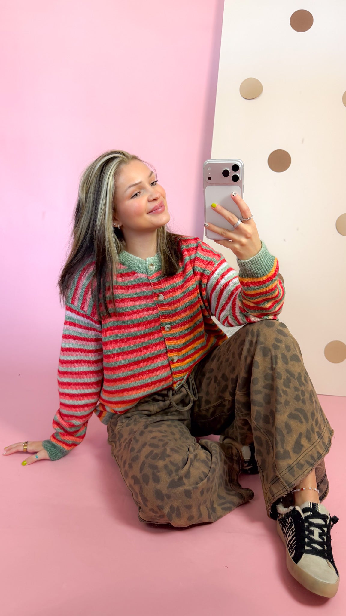 Seated mirror view of Christmas space-dye striped cardigan showing button front and green ribbed cuffs