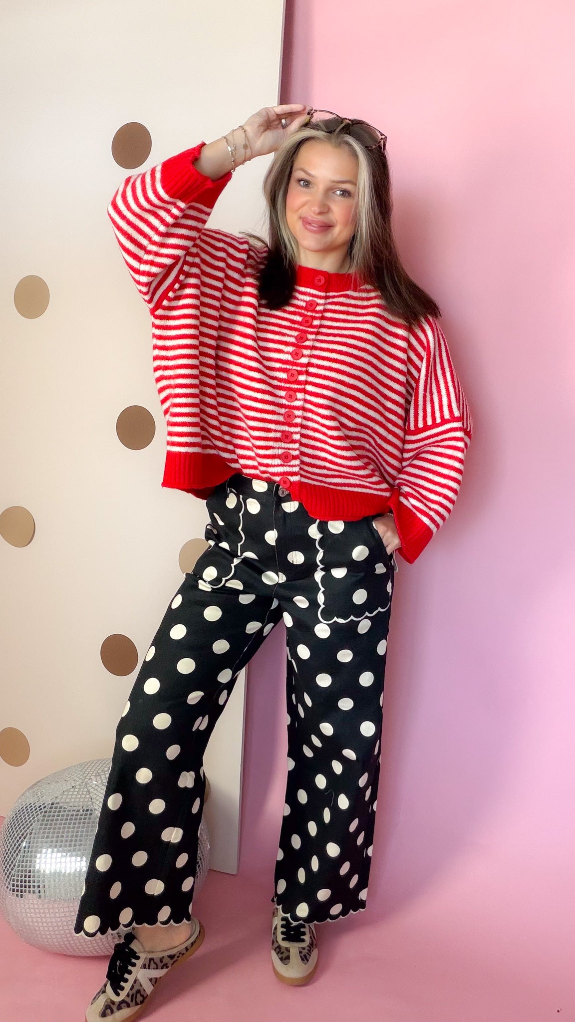 Full outfit with red and ivory striped button sweater, black polka-dot wide-leg pants, and patterned sneakers.