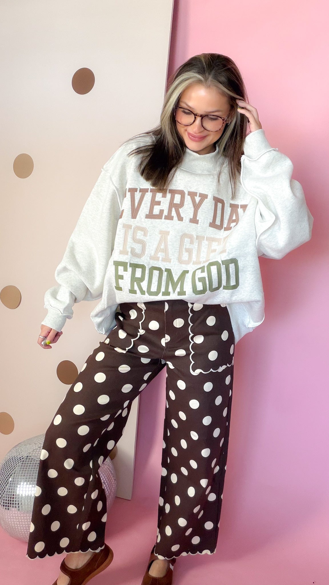 Brown polka dot wide leg pants styled with a cream graphic sweatshirt and brown Mary Jane flats.