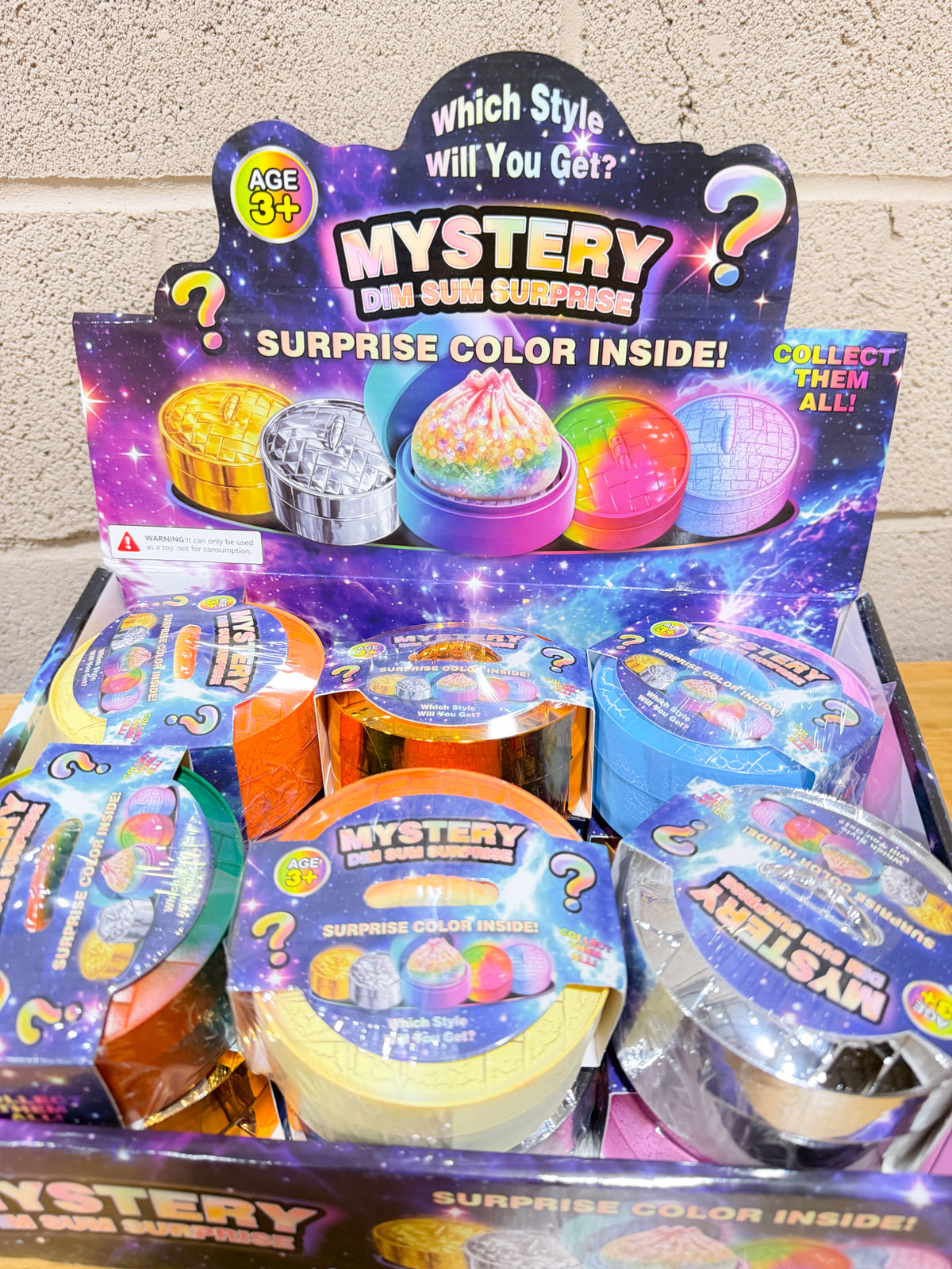 Close-up of colorful round Mystery Dim Sum Surprise packages in a purple galaxy-themed display marked ages 3+.