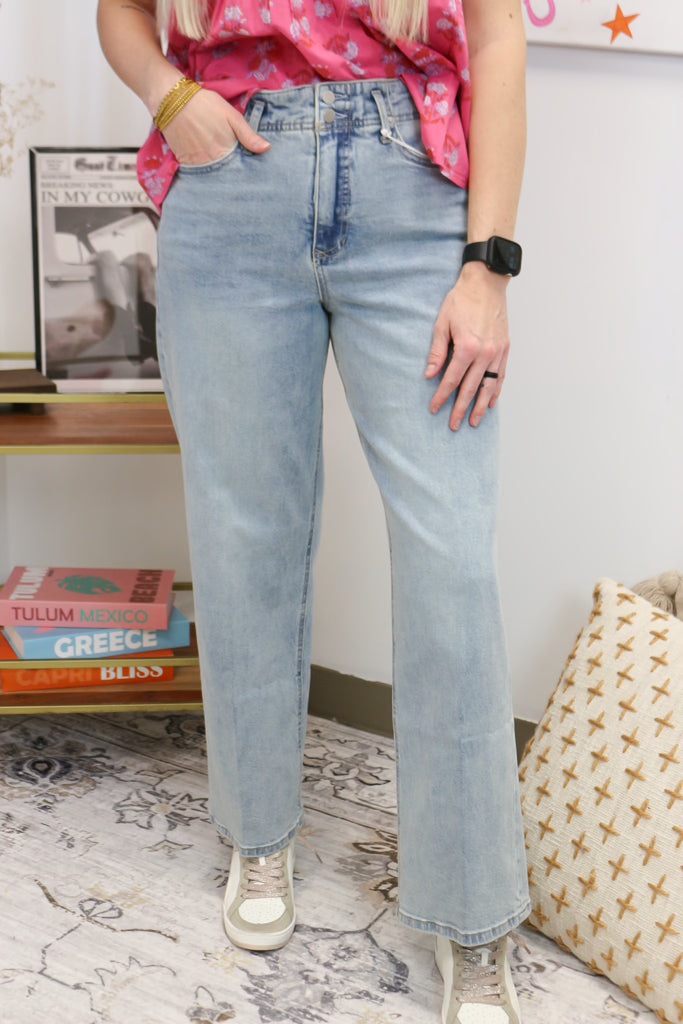 Person wearing light blue jeans in a room with books and a patterned rug.