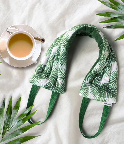 Hot Stuff Heated Neck Wrap in green palm leaf print, laid out next to a cup of tea