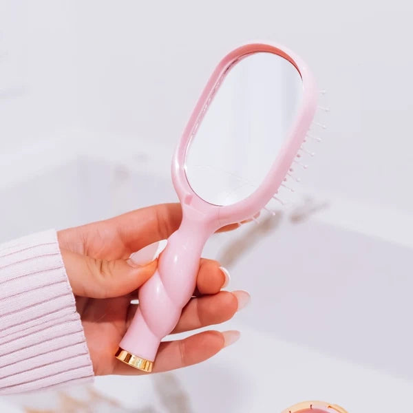 Hand holding the Teleties Mini Detangler Brush in Bubblegum Pink showing its built-in mirror