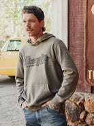 Wrangler Legacy script graphic hoodie in olive, worn by man outdoors by a truck