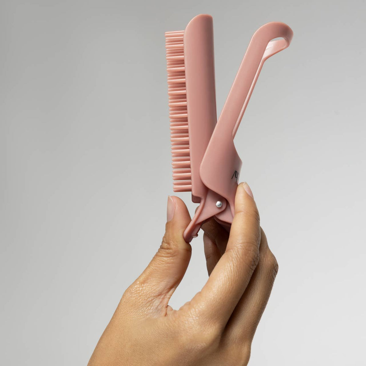 Hand opening a terracotta Kitsch Hair Volumizing Clip to show the comb teeth