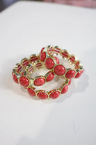 A stack of three gold-plated stretch bracelets, each featuring a row of oval red cabochon stones, displayed on a white surface.