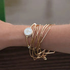 Beloved Tap To Pray gold-tone beaded cross bracelet worn on a wrist with layered gold-tone bracelets.