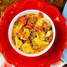 Bowl of Crockstar sausage and cheese tortellini with tomatoes, served on a red plate