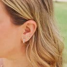 Medium Esther gold-tone huggie earring worn on an ear alongside small gold-tone studs.