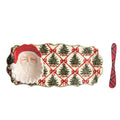 A Christmas-themed serving tray with a 3D Santa face on one end, a red Santa hat, and a pattern of green Christmas trees tied with red bows on a cream background. A red and black plaid napkin is placed to the right of the tray on a plain white background.