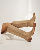 Pair of beige knee-high boots with brown soles on a white background. Tecovas women’s cowboy boots
