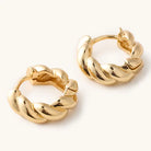 Gold croissant huggie earrings with rounded twisted ridges and hinged closures on a light background.