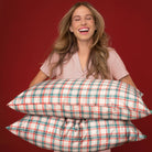 Kitsch holiday plaid satin pillowcases on two stacked pillows held by a laughing model