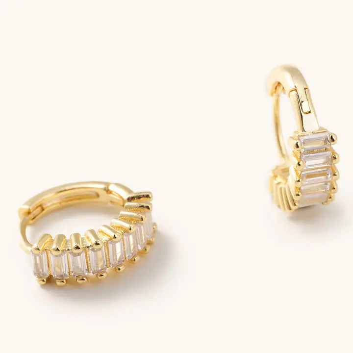 Side views of Medium Esther gold-tone huggie hoops showing clear rectangular stones and hinged closures.