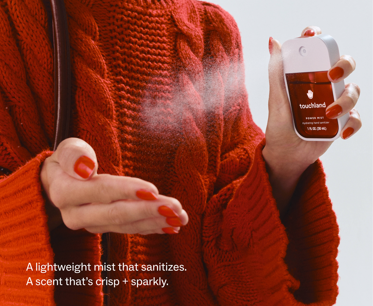 Touchland Cranberry Fizz Power Mist being sprayed onto a hand, red sweater background