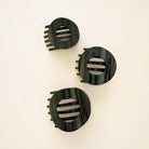 Three Teleties Jet Black Medium Flat Circle Hair Clips on a cream surface
