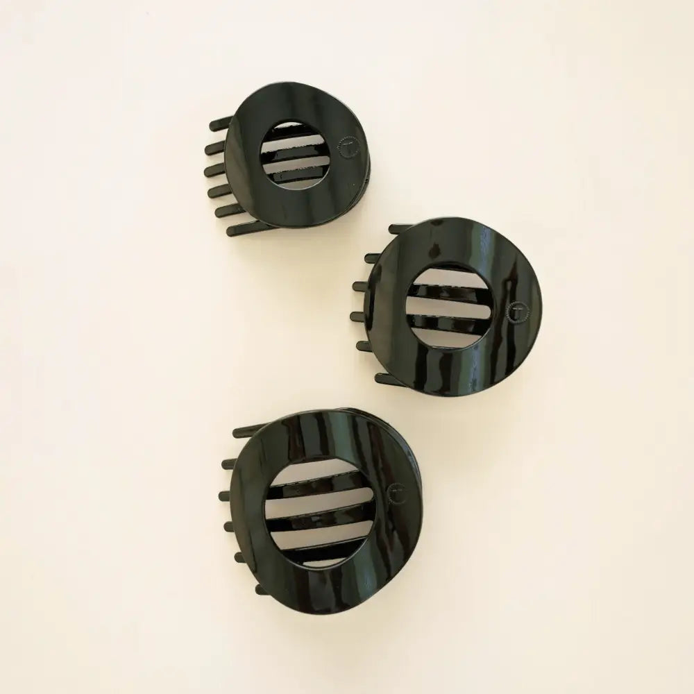 Three Teleties Jet Black Small Flat Circle Hair Clips on a cream surface