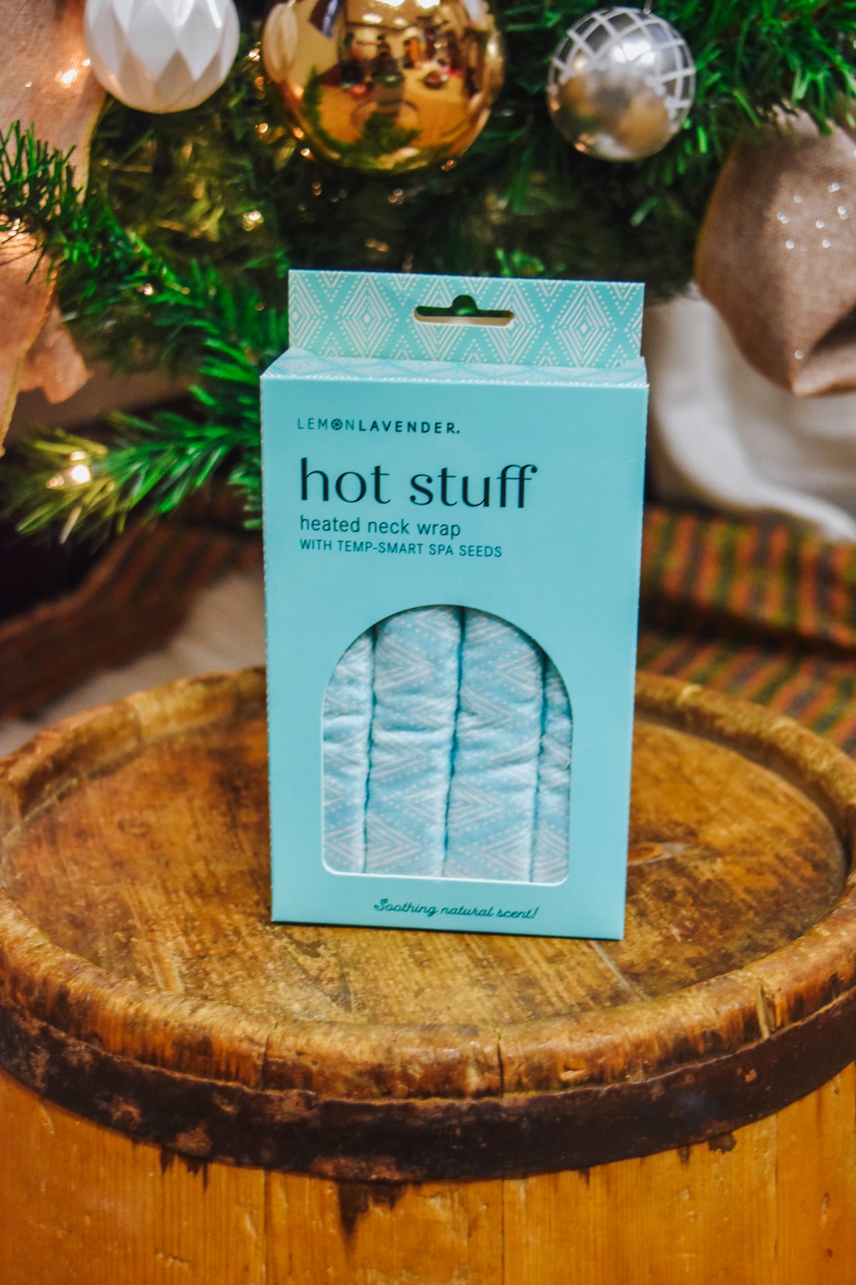 Lemon Lavender Hot Stuff Heated Neck Wrap in light blue, boxed by a Christmas tree