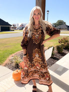 Model poses with hand on hip wearing a brown floral midi dress with a scalloped ruffle border hem