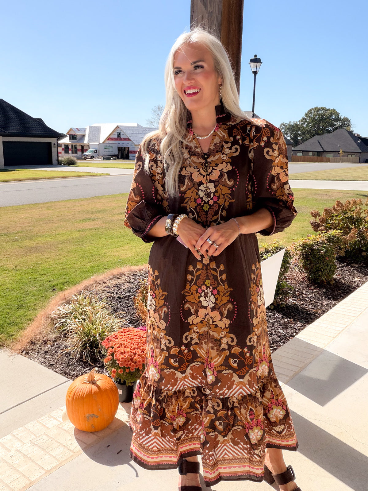 Model in a brown floral print midi dress featuring a ruffle stand collar and bracelet stack