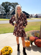 Front view of merlot floral smocked dress with long sleeves and ruffled hem, styled with dark boots