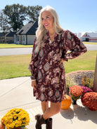 Angled front view of merlot floral smocked dress, model posing with one hand on hip and dark boots