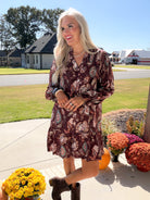 Merlot floral button-down dress with long gathered sleeves and ruffled hem, model with hands at waist