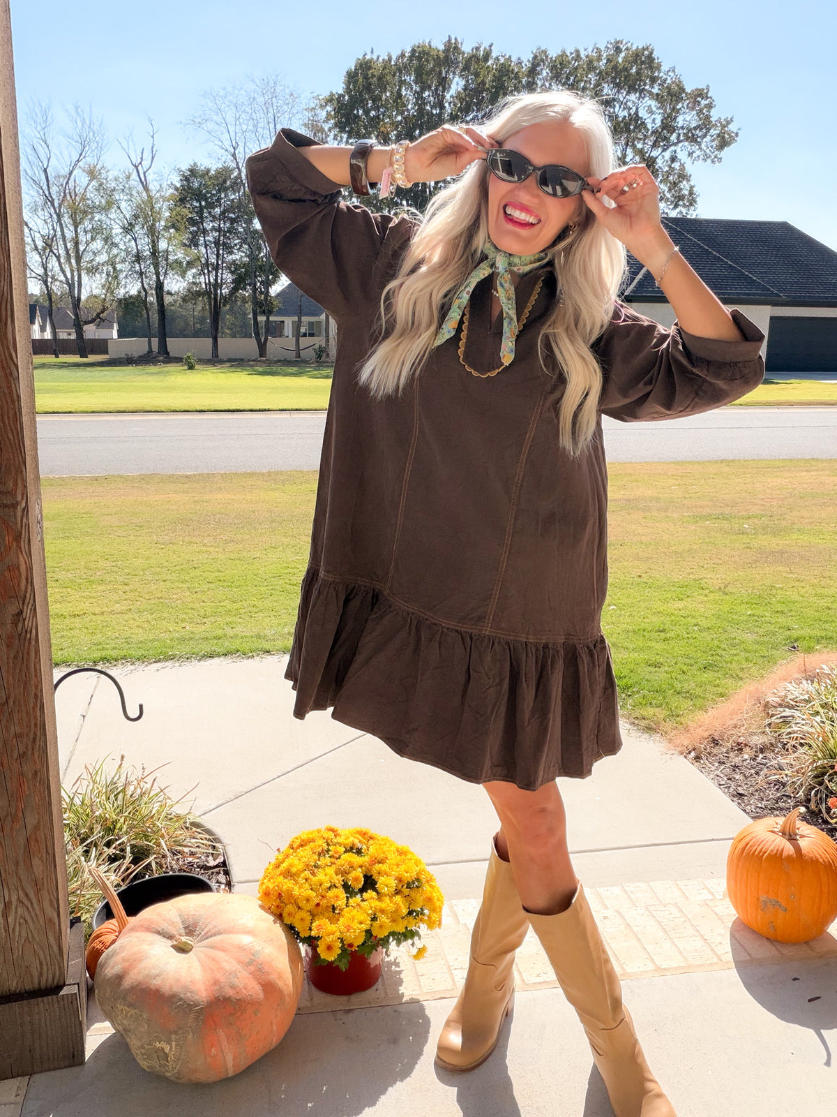 Front view of chocolate brown corduroy dress with tiered ruffle hem, model adjusting sunglasses