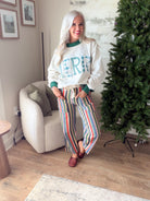 Women's ivory MERRY Christmas sweatshirt with green collar and cuffs, styled with striped pants and woven mules.