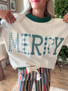 Close-up of plaid and polka dot MERRY letter appliqués and green mock neckline on an ivory Christmas sweatshirt.